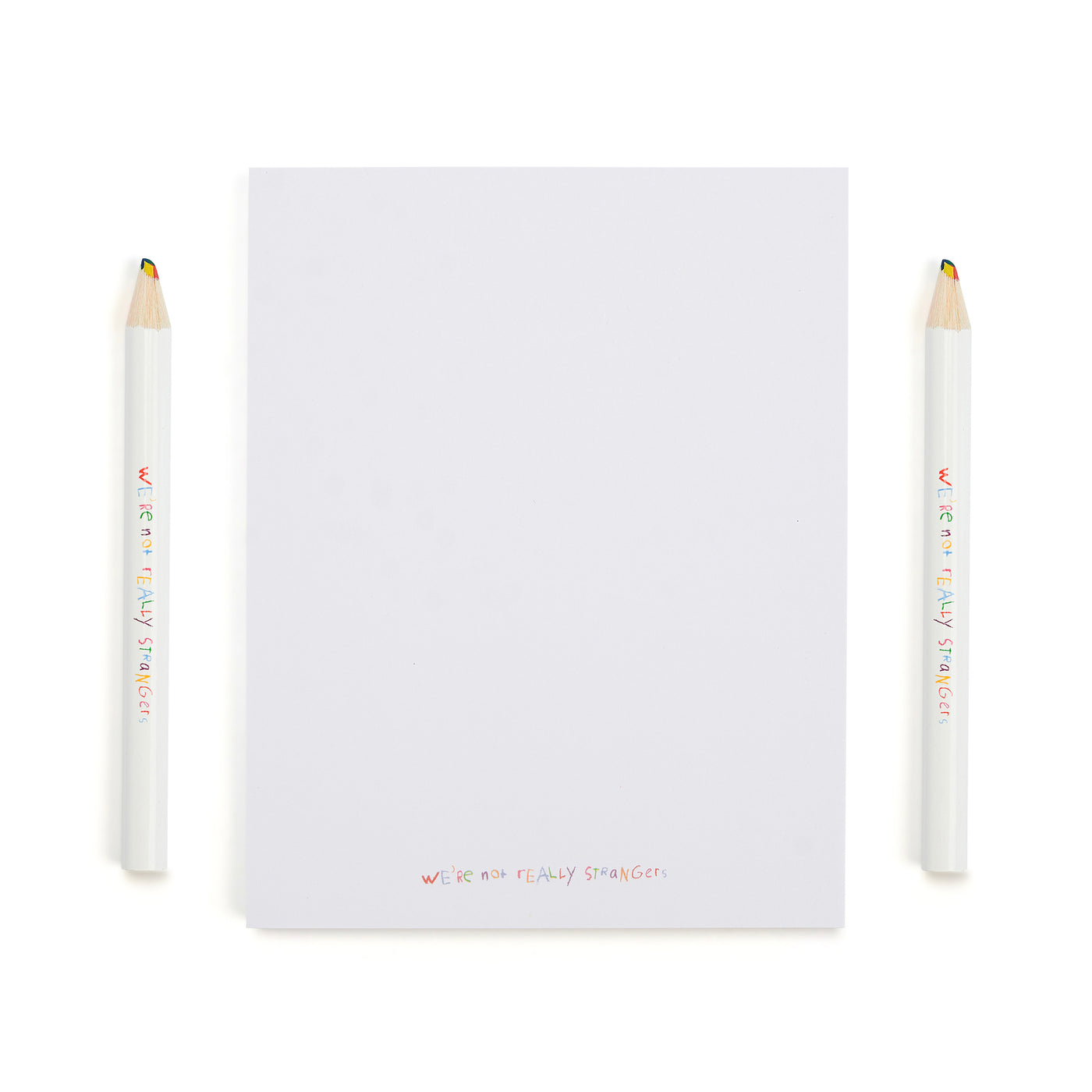 We're Not Really Strangers Kids Edition. Front facing view of Kids Edition white notepad and 2 rainbow colored pencils.